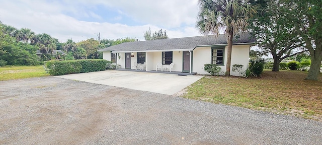 ranch-style home with a front yard, covered porch, concrete driveway, stucco siding, and roof with shingles