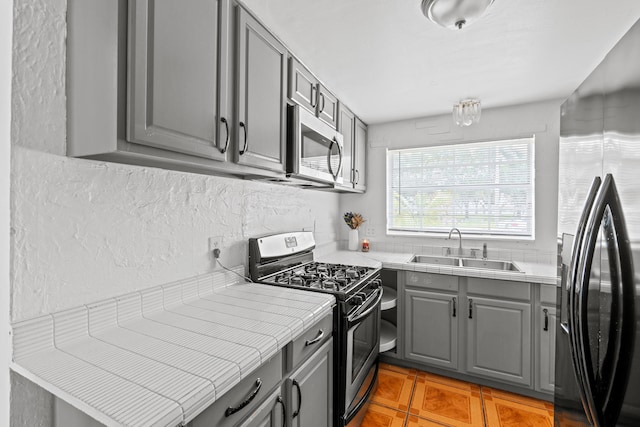 3700 N Australian Ave, West Palm Beach, FL 33407 - kitchen featuring gray cabinetry, stainless steel appliances, a sink, tile countertops, and light tile patterned floors