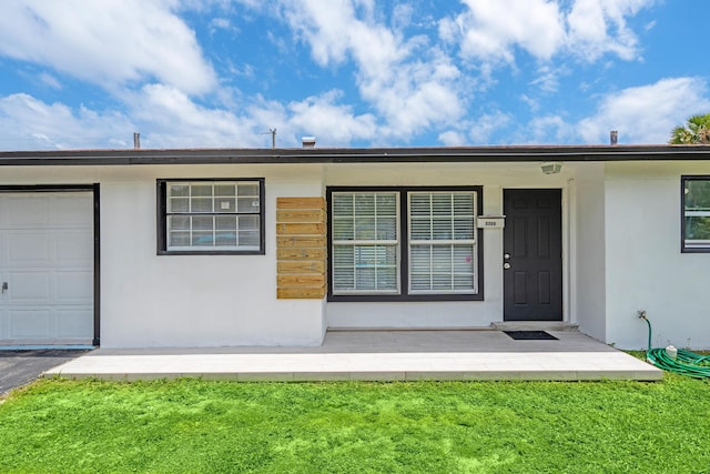 3700 N Australian Ave, West Palm Beach, FL 33407 - view of exterior entry with stucco siding, a yard, and an attached garage
