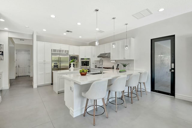 kitchen featuring built in appliances, a peninsula, under cabinet range hood, visible vents, and a breakfast bar area