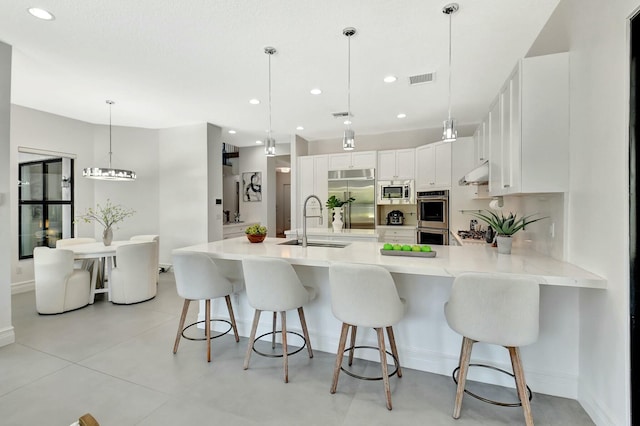 kitchen with white cabinets, built in appliances, a sink, light countertops, and a peninsula