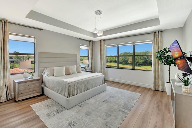 bedroom with a raised ceiling, baseboards, and light wood-style flooring