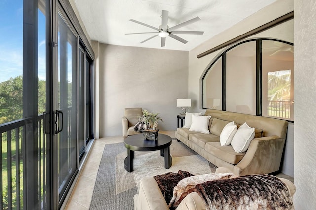 living area with a textured wall, light tile patterned floors, and a ceiling fan