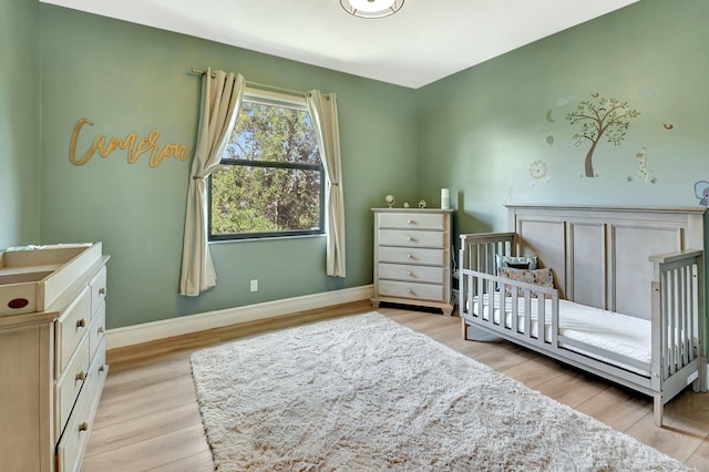 bedroom featuring a crib, light wood finished floors, and baseboards