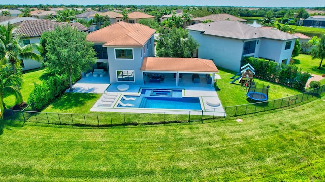 rear view of house with a hot tub, a lawn, a fenced backyard, a tile roof, and a playground