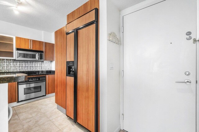 1551 N Flagler Dr Unit 1509, West Palm Beach, FL 33401 - kitchen with a textured ceiling, brown cabinets, dark stone counters, stainless steel appliances, and decorative backsplash