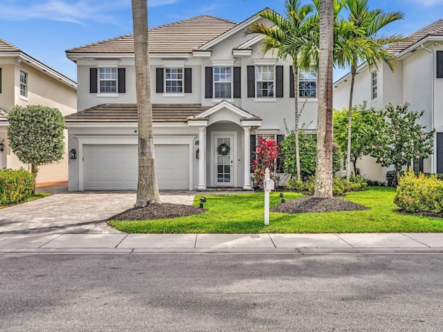 view of front facade featuring stucco siding, a front yard, a tile roof, an attached garage, and driveway