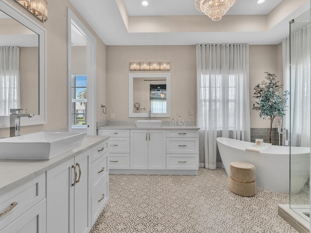 bathroom featuring a freestanding bath, two vanities, a sink, and a raised ceiling