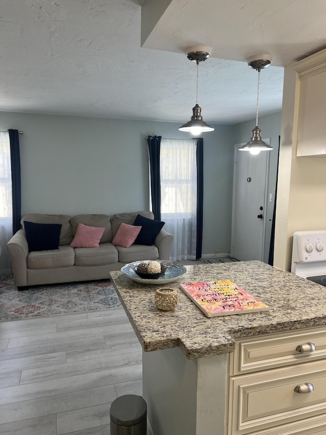 kitchen featuring light stone countertops, stove, light wood-style flooring, hanging light fixtures, and open floor plan