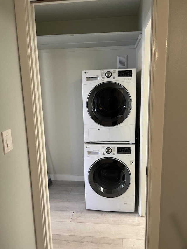 laundry room with baseboards, stacked washing maching and dryer, visible vents, laundry area, and wood finished floors