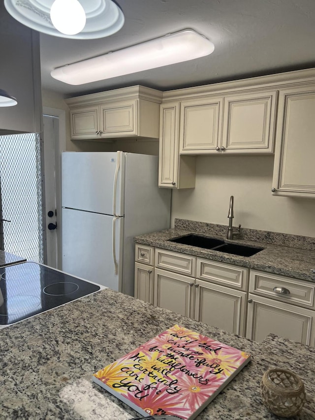 kitchen with freestanding refrigerator, a sink, cream cabinetry, and dark stone counters