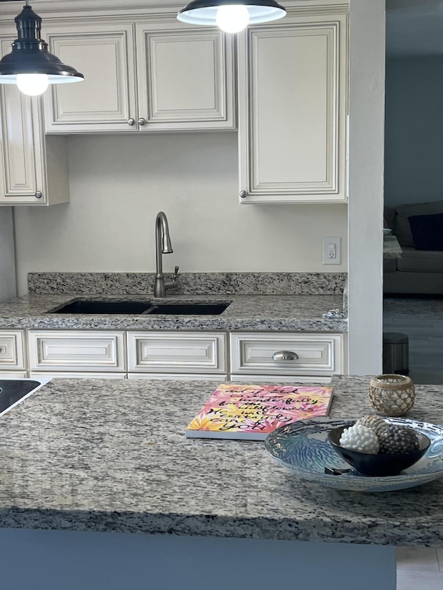 kitchen featuring white cabinets, decorative light fixtures, a sink, and light stone counters