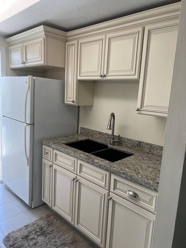 kitchen with dark stone countertops, light tile patterned floors, cream cabinets, freestanding refrigerator, and a sink