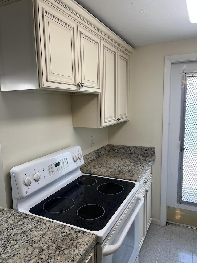kitchen with electric stove, baseboards, and cream cabinetry
