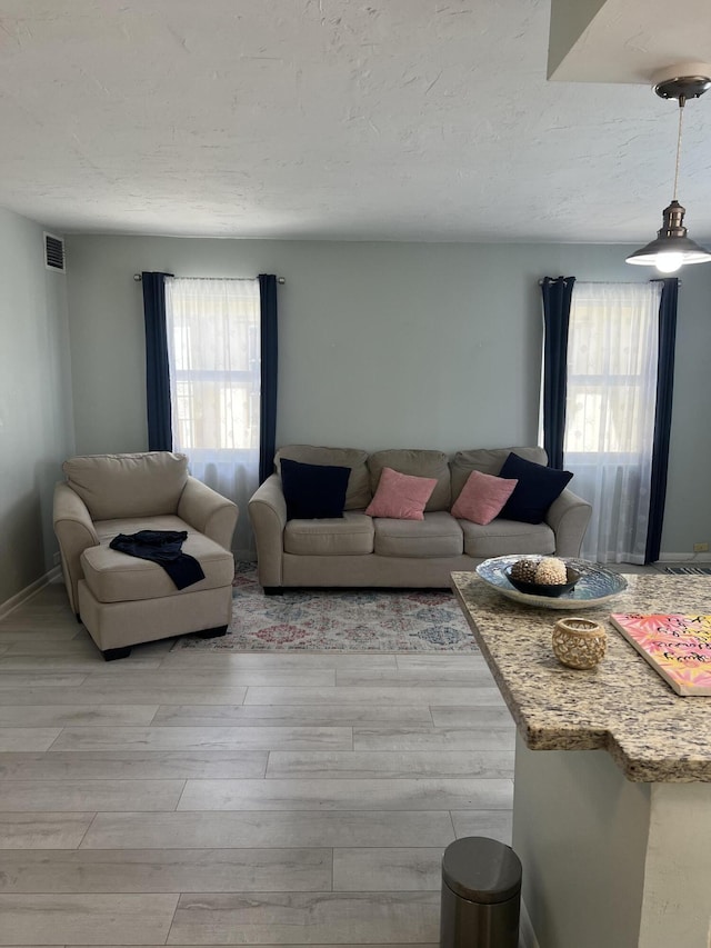 living area with baseboards, light wood-style floors, a textured ceiling, and visible vents