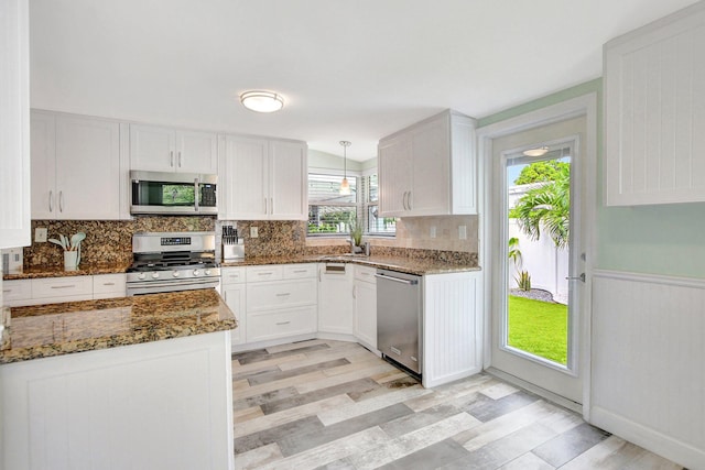 kitchen with dark stone countertops, light wood-style flooring, white cabinetry, backsplash, and appliances with stainless steel finishes