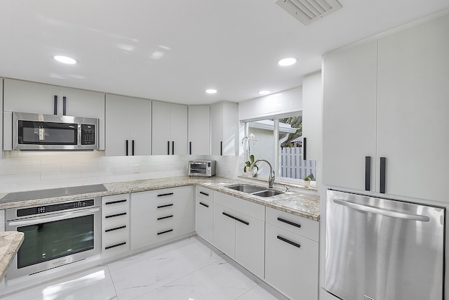 1900 NE 16th Ter, Fort Lauderdale, FL 33305 - kitchen with visible vents, a sink, appliances with stainless steel finishes, backsplash, and light stone counters