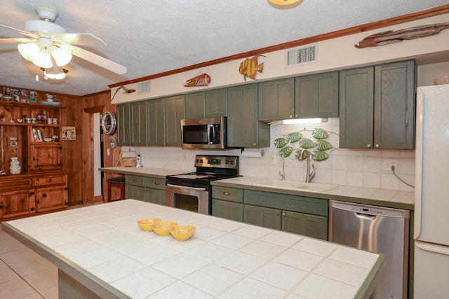kitchen featuring decorative backsplash, a ceiling fan, tile counters, a sink, and appliances with stainless steel finishes