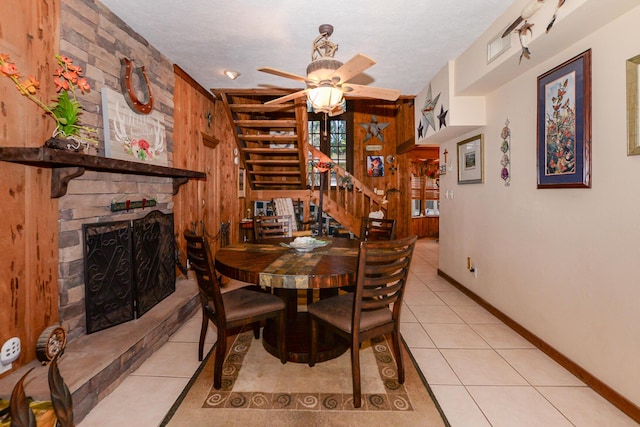 dining area with a ceiling fan, a fireplace, stairway, baseboards, and light tile patterned flooring