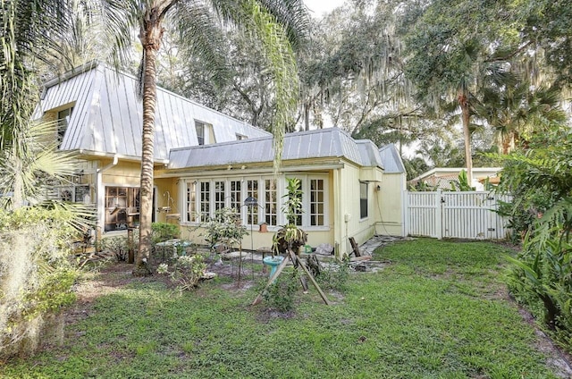 rear view of house with a yard, fence, metal roof, and a gate