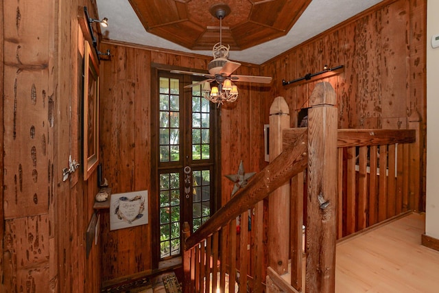 stairs with wooden walls, crown molding, a barn door, a ceiling fan, and wood finished floors