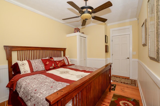 bedroom featuring crown molding, light wood-style flooring, wainscoting, and a closet
