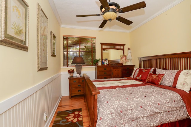 bedroom featuring a wainscoted wall, ornamental molding, a ceiling fan, and wood finished floors