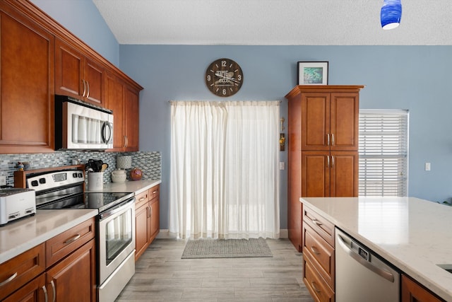 1103 Aviary Rd, Wellington, FL 33414 - kitchen featuring light wood-style floors, a textured ceiling, brown cabinetry, stainless steel appliances, and backsplash