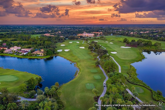 aerial view at dusk featuring a water view and view of golf course