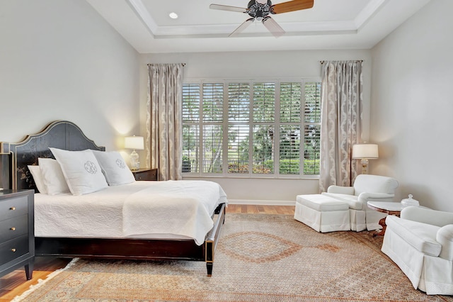 bedroom featuring ceiling fan, baseboards, wood finished floors, and a tray ceiling