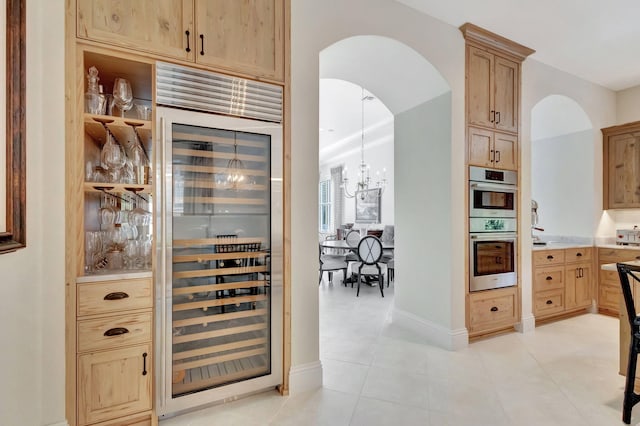 bar featuring light tile patterned floors, wine cooler, baseboards, double oven, and arched walkways