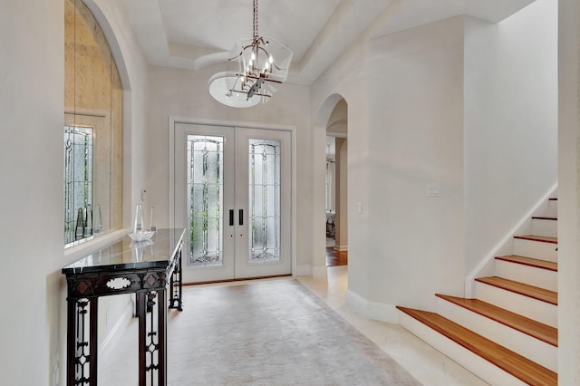 entrance foyer with arched walkways, a towering ceiling, french doors, a notable chandelier, and stairs