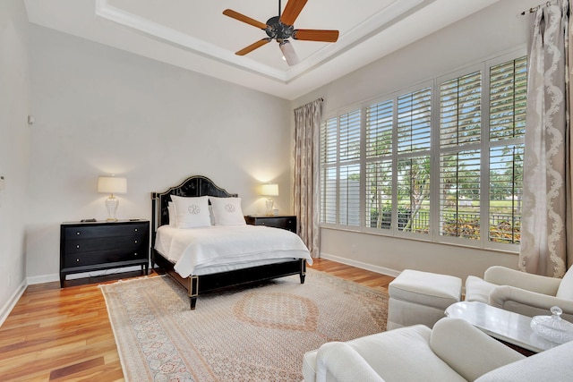 bedroom featuring baseboards, light wood-style floors, and a tray ceiling