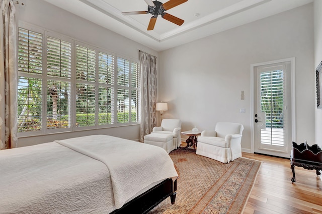 bedroom with hardwood / wood-style floors, access to exterior, ceiling fan, baseboards, and a tray ceiling