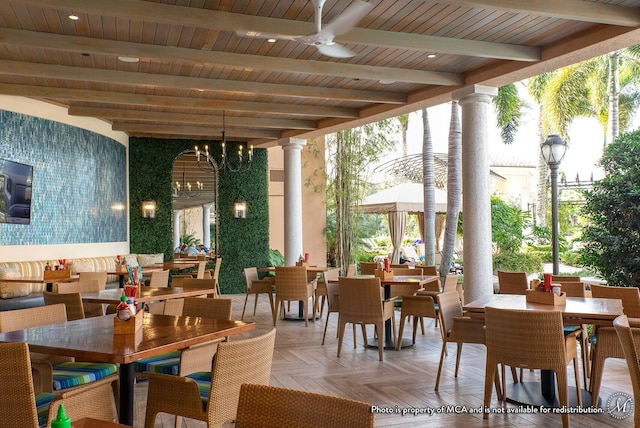 dining space featuring ceiling fan with notable chandelier, wooden ceiling, beamed ceiling, and ornate columns