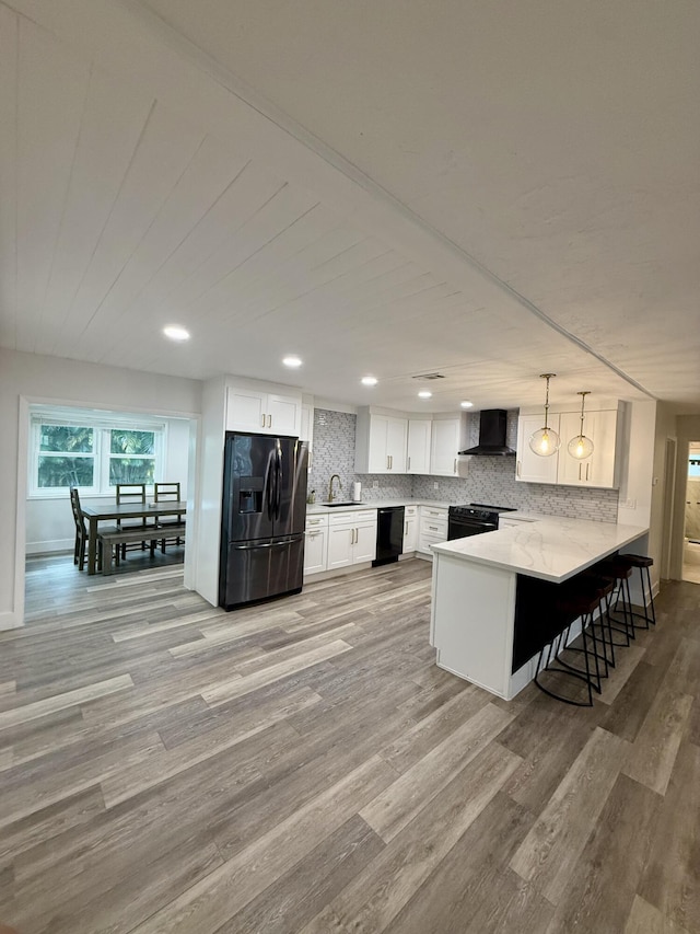 kitchen with wall chimney exhaust hood, a sink, light wood-style floors, a peninsula, and black appliances