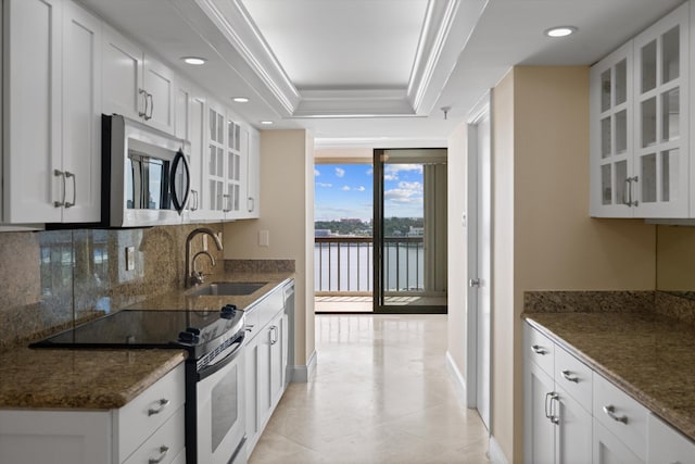 kitchen with a sink, decorative backsplash, range with electric cooktop, a tray ceiling, and stainless steel microwave