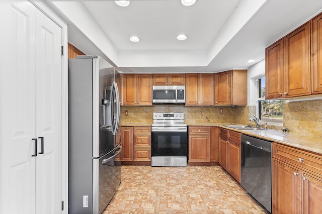 kitchen featuring brown cabinetry, a sink, backsplash, and stainless steel appliances