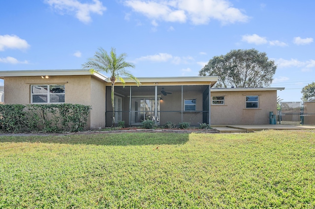 rear view of property featuring a sunroom, a yard, a ceiling fan, stucco siding, and fence