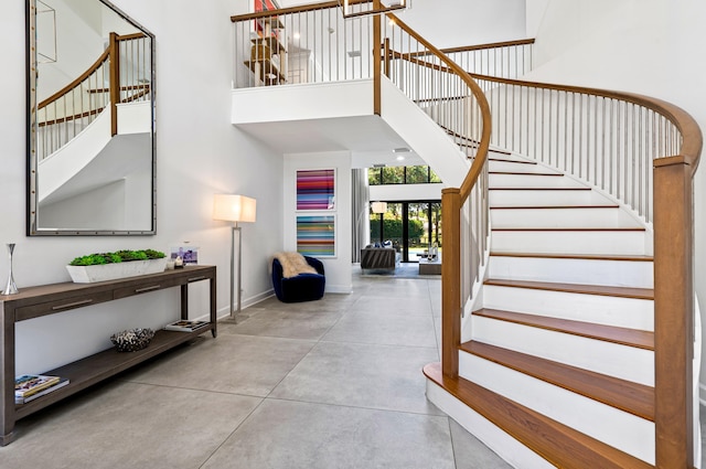 entryway with stairway, concrete flooring, a high ceiling, and baseboards