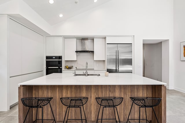 kitchen featuring wall chimney range hood, a sink, modern cabinets, white cabinets, and stainless steel built in refrigerator