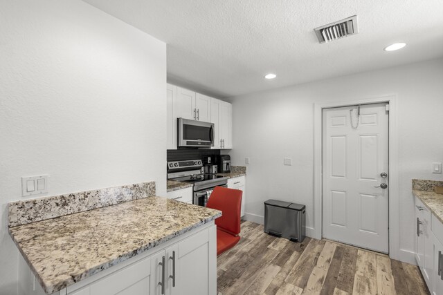 944 Hansen St, West Palm Beach, FL 33405 - kitchen with stainless steel appliances, white cabinets, light wood-type flooring, light stone countertops, and recessed lighting