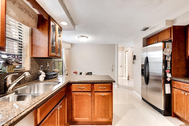 kitchen with stainless steel fridge with ice dispenser, a peninsula, a textured ceiling, visible vents, and a sink