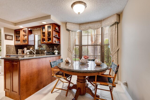 dining room with indoor wet bar, a textured ceiling, light tile patterned floors, and baseboards