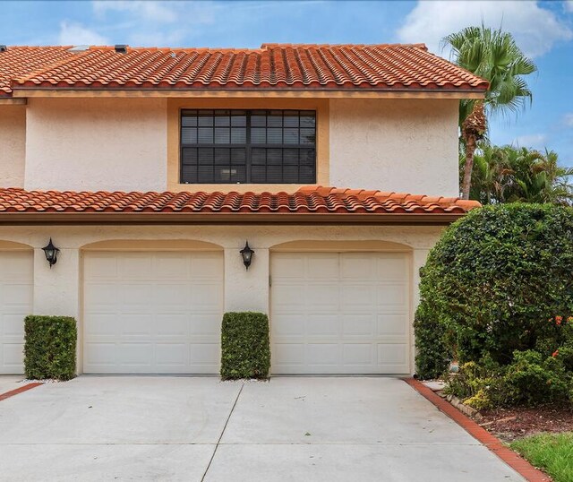 mediterranean / spanish house featuring driveway, a tile roof, a garage, and stucco siding