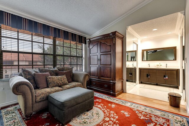 sitting room with ornamental molding, baseboards, light wood-type flooring, and a textured ceiling