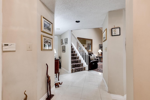 corridor with stairway, a textured ceiling, baseboards, and light tile patterned flooring