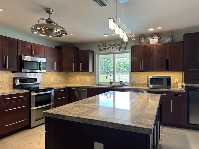 kitchen with a sink, a kitchen island, light tile patterned floors, and appliances with stainless steel finishes