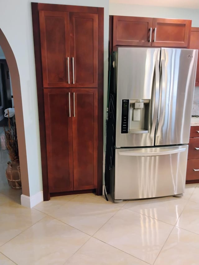kitchen with arched walkways, reddish brown cabinets, stainless steel fridge with ice dispenser, and light tile patterned flooring