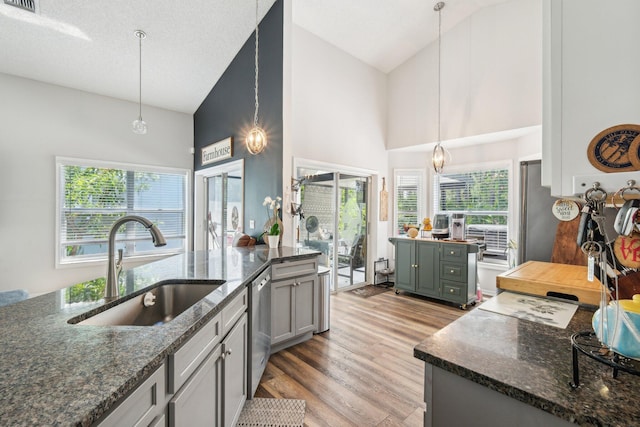 kitchen with light wood-style floors, high vaulted ceiling, dark stone counters, a sink, and dishwasher